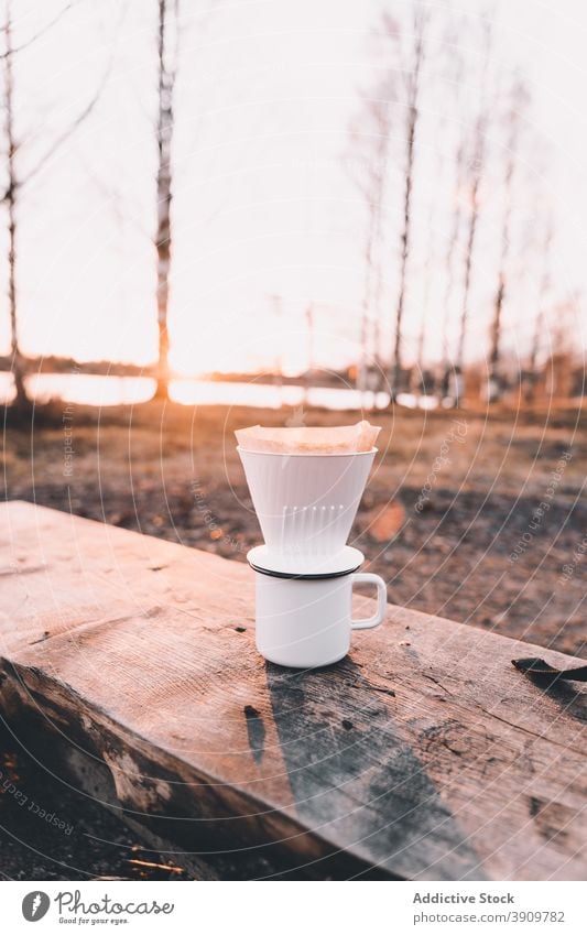 Metal mug with V60 coffee maker on wooden bench in forest v60 cup cozy campsite drink coffeemaker woods plastic metal nature cold season sunset winter beverage