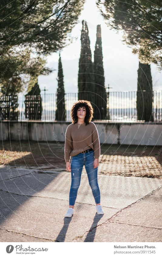 Beautiful female with curly hair in a park wearing a beige sweater and jeans with white sneakers. sunlight fashion portrait afro woman real woman human being