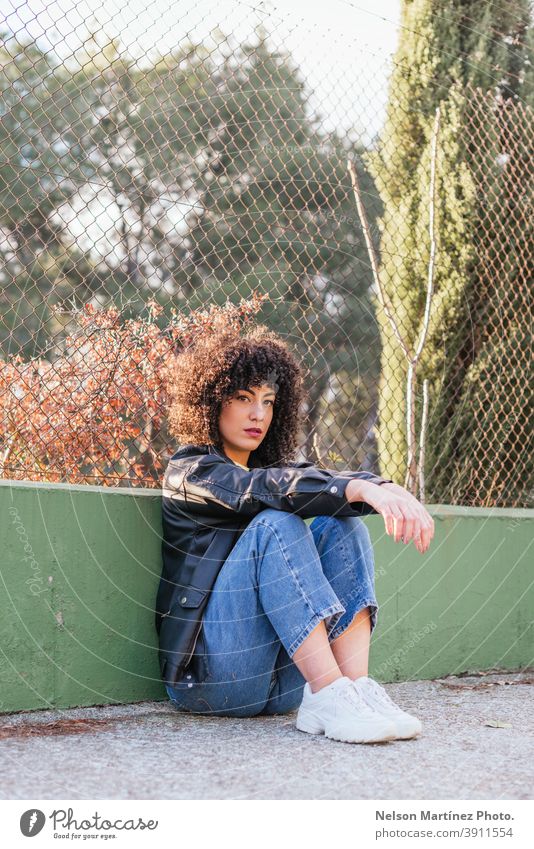 Beautiful female with curly hair in a park wearing a leather jacket and white sneakers. sunlight fashion portrait afro woman real woman human being ethnicity