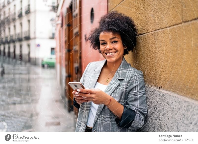 Pretty Afro Woman Using Phone looking at camera woman afro portrait black woman using phone street city life smiling cellphone smartphone communication