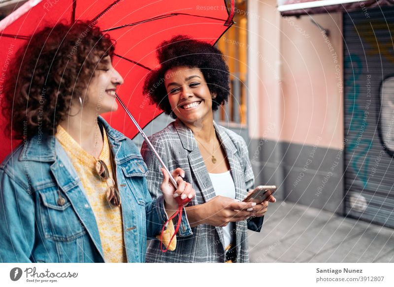 Happy Friends in Rainy Day umbrella rainy day friends afro girl black woman caucasian using phone city life smiling side view portrait women