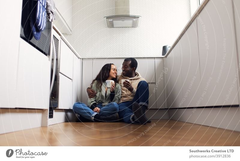 Young Couple Celebrate Moving Into New Home Sitting On Floor With Hot Drink In Kitchen couple young couple house buying drink drinking hot drink takeaway