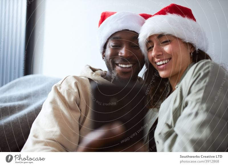 Young Smiling Couple Wearing Santa Hats At Home Posing For Christmas Selfie On Mobile Phone Together couple young couple at home posing selfie christmas santa