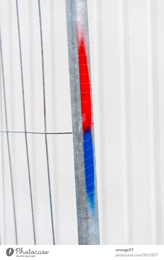 Red and blue color marking on a construction fence in front of a light gray container in the background Hoarding Blue red and blue marking reddish blue label