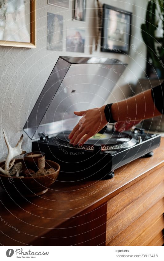 Woman with fitness bracelet puts a record on her record player in a cozy home disk Record player place a record Cozy Wood interior Lifestyle furnishing