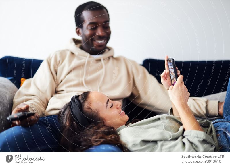 Relaxed Young Couple At Home Sitting On Sofa Watching TV And Checking Social Media On Mobile Phone couple young couple at home sitting sofa lounge watching tv
