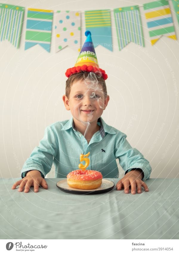 Child through smoke from candle on festive donut birthday boy hands five year his little smiling child hold plate doughnut looking at camera smile fun