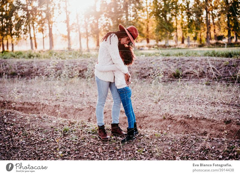 portrait of hispanic mother and afro kid girl hugging outdoors at sunset during golden hour. Autumn season. Family concept kiss woman daughter nature family