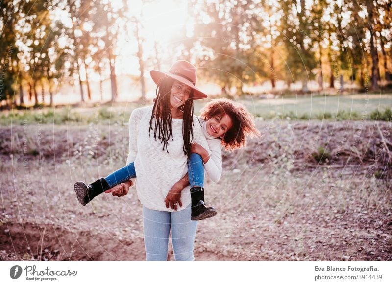 portrait of hispanic mother and afro kid girl playing outdoors at sunset during golden hour. Autumn season. Family concept woman daughter nature family love