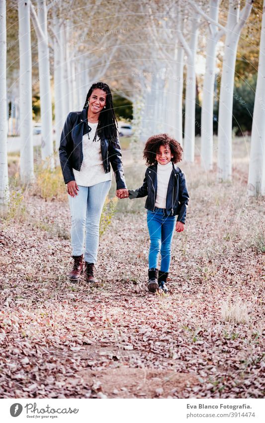 hispanic mother and afro kid girl outdoors walking at sunset by path of trees. Autumn season. Family and love concept hug family woman daughter nature together