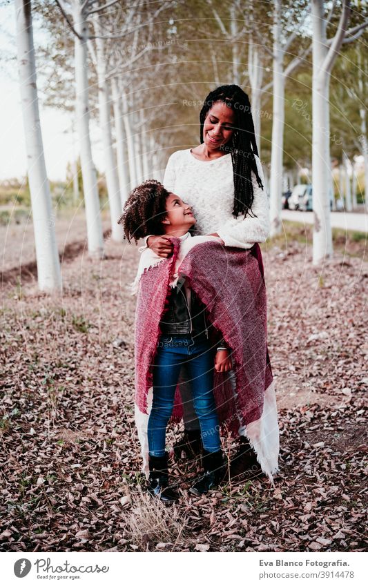 hispanic mother and afro kid girl outdoors hugging at sunset wrapped in blanket. Autumn season. Family and love concept family woman daughter nature together