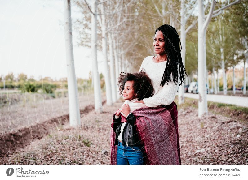 hispanic mother and afro kid girl outdoors hugging at sunset wrapped in blanket. Autumn season. Family and love concept family woman daughter nature together