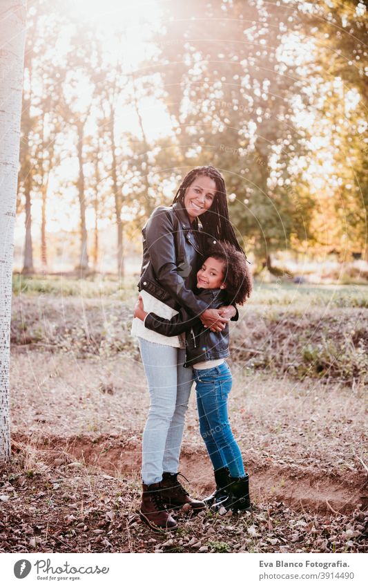 hispanic mother and afro kid girl outdoors hugging at sunset during golden hour. Autumn season. Family and love concept family woman daughter nature together