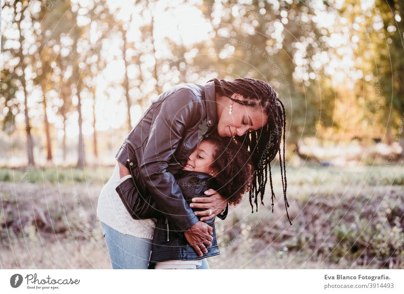 hispanic mother and afro kid girl outdoors hugging at sunset during golden hour. Autumn season. Family and love concept family woman daughter nature together