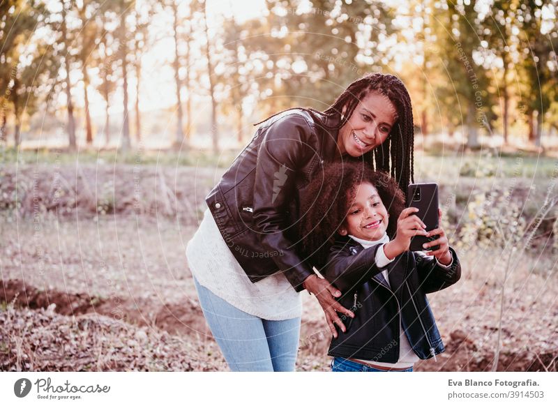 hispanic mother and cute afro kid girl taking selfie outdoors at sunset. Family, love and technology concept mobile phone family device hug woman daughter
