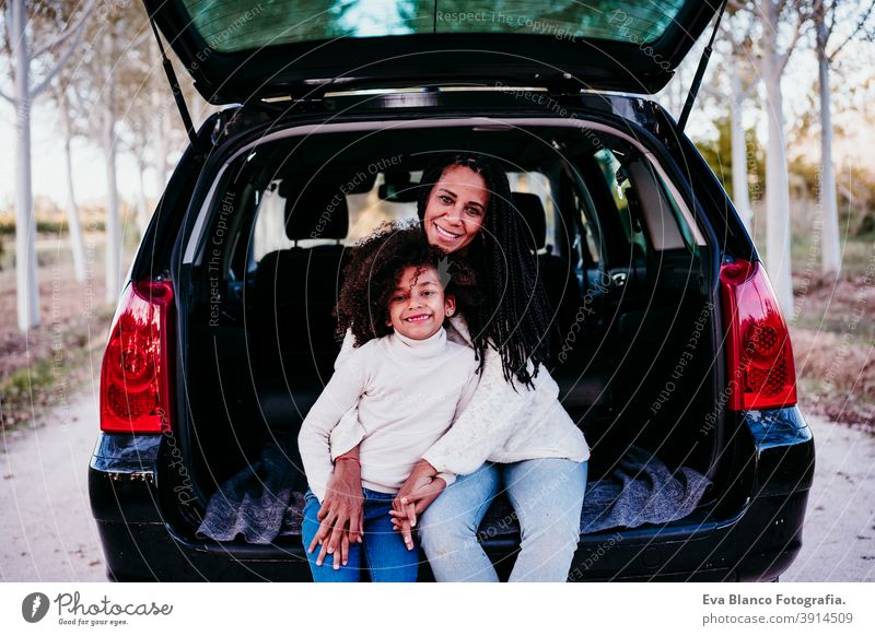 hispanic mother and afro kid girl sitting in a car in nature. Autumn season. Family and travel concept portrait daughter family outdoors mixed race motherhood