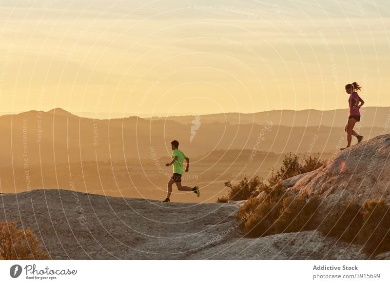 Young runners training in mountains at sunset together sportspeople cardio sunlight athlete highland terrain sportsman sportswoman slope sportswear wellbeing
