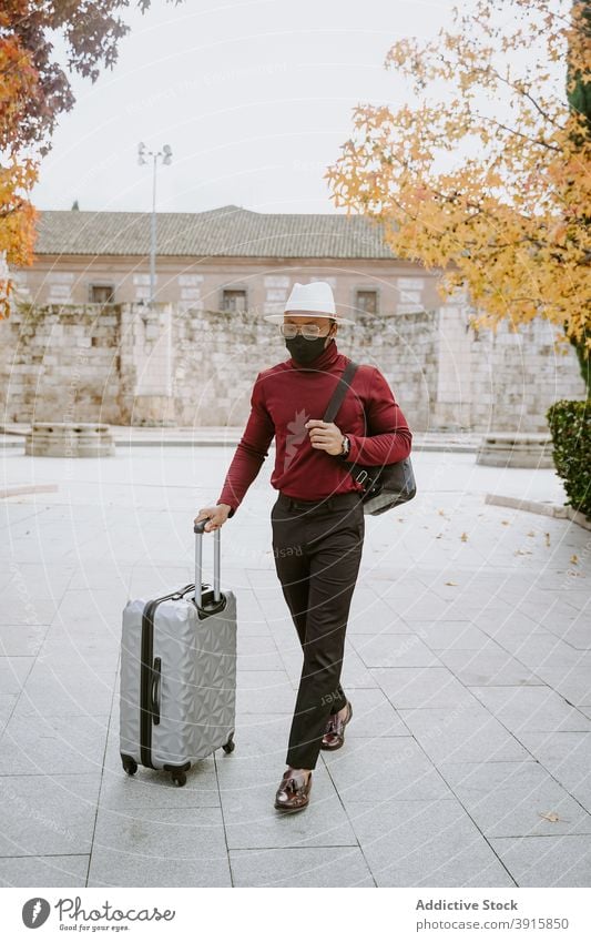 Traveling black man in mask walking in city with suitcase traveler luggage elegant baggage arrive tourist male ethnic african american new normal protect covid