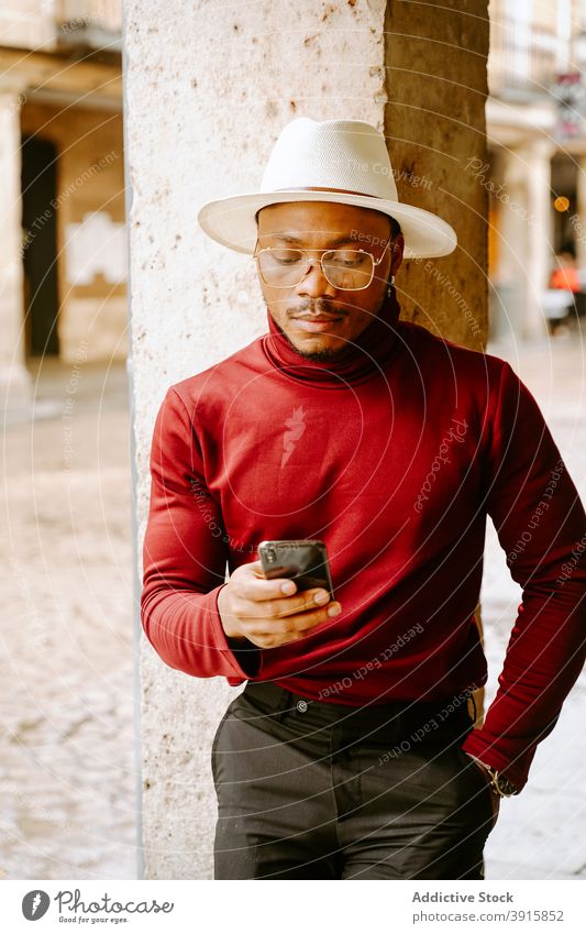 Black man in stylish outfit using mobile phone in city elegant smartphone style street determine trendy hat male ethnic browsing message black african american