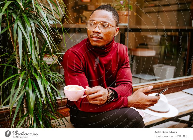 Black man browsing on smartphone drinking coffee near cafe in city surfing social media street style trendy male ethnic black african american internet