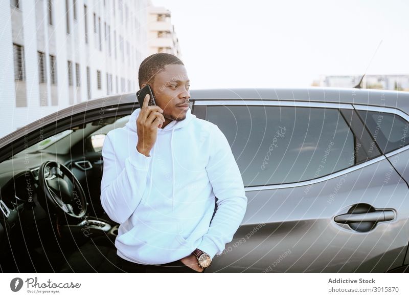 Black man browsing smartphone near car parked surfing social media internet male ethnic black african american rich expensive luxury posh mobile phone journey