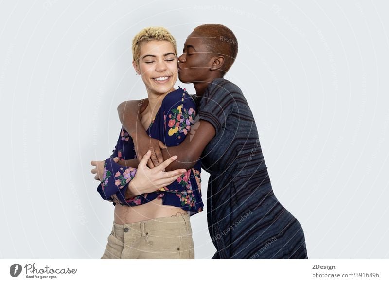 Photo of joyful ladies kissing and embracing togetherness, being of different of races, dressed in casual jumpers, isolated over white background. couple