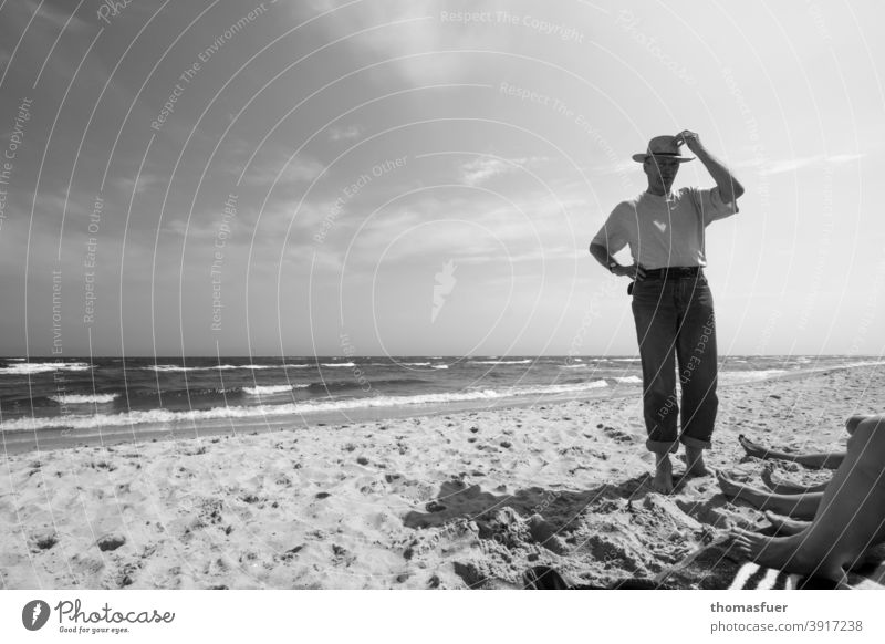 Man with hat on the beach and feet of some ladies Hat clad Pants T-shirt Beach Ocean Waves leg Wind Sun Clouds Shadow fresh from the summer wide vacation