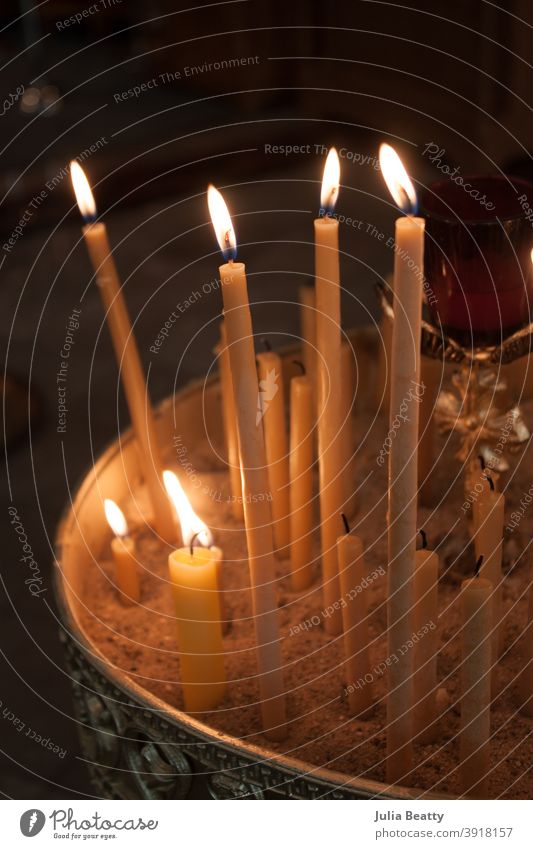 Lit beeswax candles in sand; Orthodox church lit light taper candles melt wick flame orthodox catholic prayer Candlelight Hope Church Belief Religion and faith