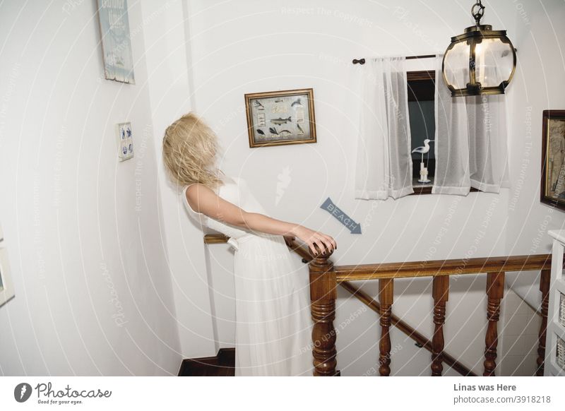 A beautiful blonde bride going downstairs at her cozy beach house. It feels like a warm home idyll. She still has a choice though. wedding dress white dress