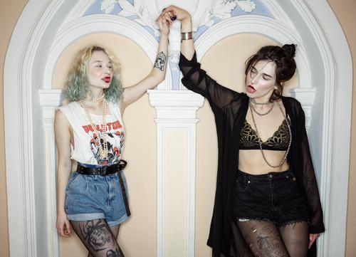Young blood and positive energy. Two wild girls with tattoos are holding hands inside a fancy mansion with a classy interior. Girls just want to have fun!