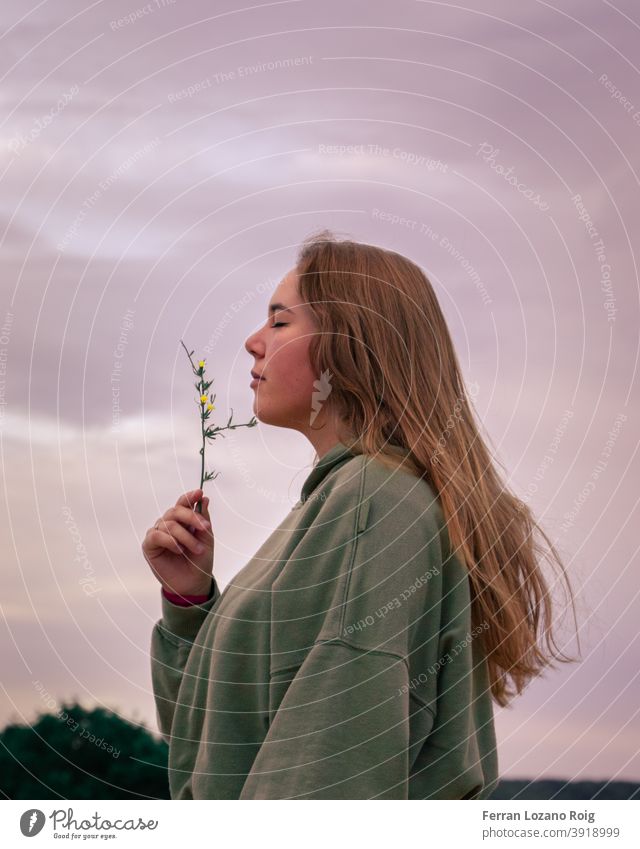 Portrait of a woman smelling a flower portrait hair brown hair long hair Closed eyes pink sky hoddie Flower flowers nature Park yellow flower yellow flowers