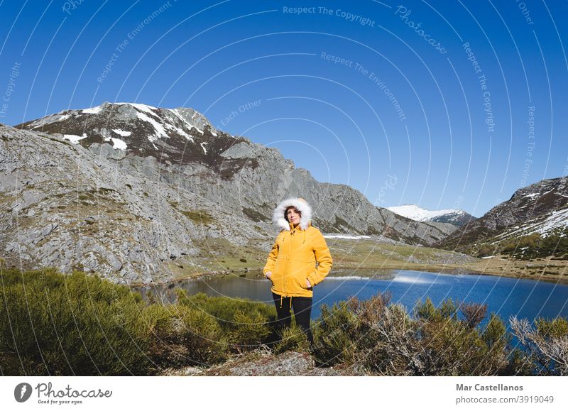 Mountain landscape with snowy mountains and lake. Woman in yellow jacket looking at camera. posed cold water limestone rock peaks nature view rocks sky shadows