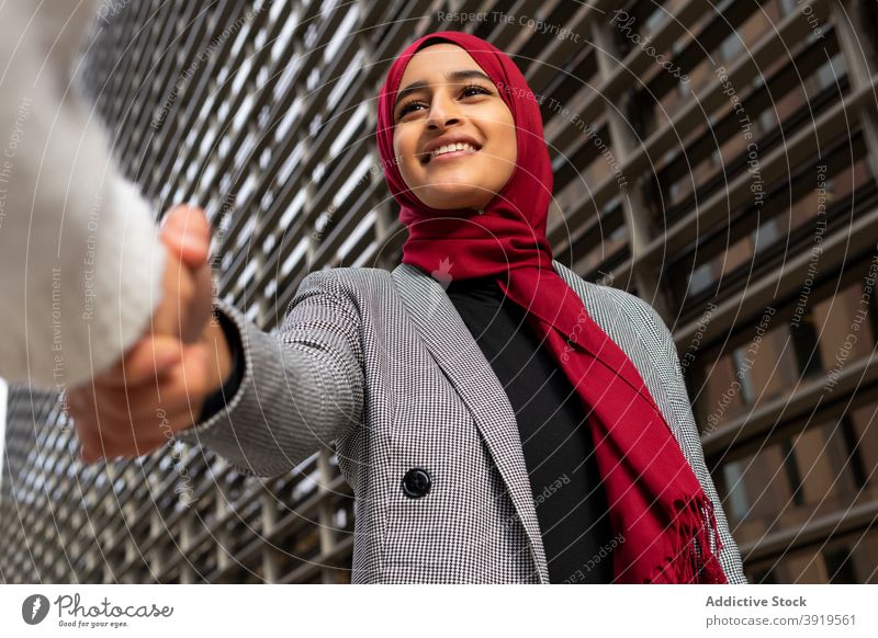 Smiling ethnic businesswoman in hijab shaking hand of partner handshake city cheerful entrepreneur headscarf tradition female arab smile job greeting optimist