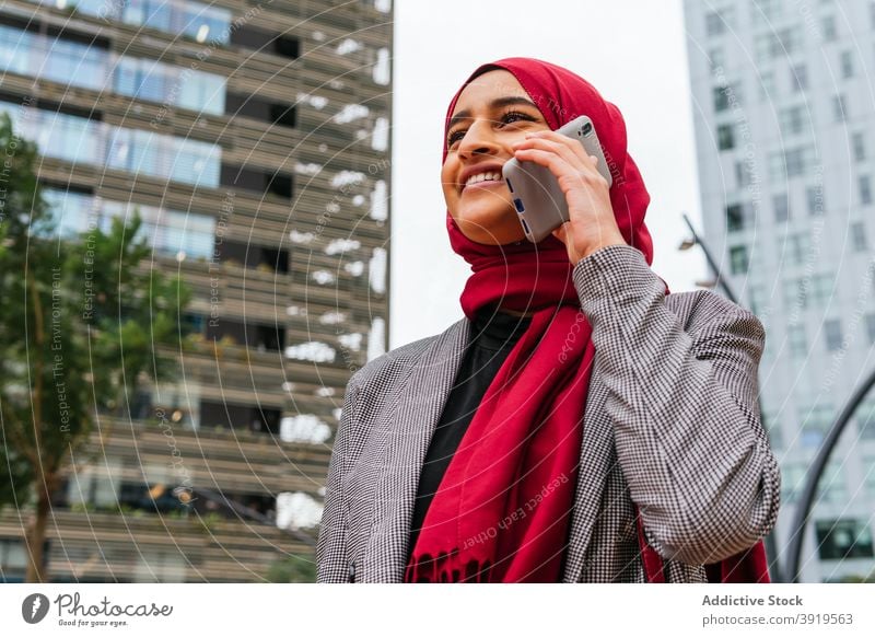 Delighted ethnic woman in hijab talking on smartphone in city headscarf cheerful speak tradition street female arab mobile using conversation device call happy