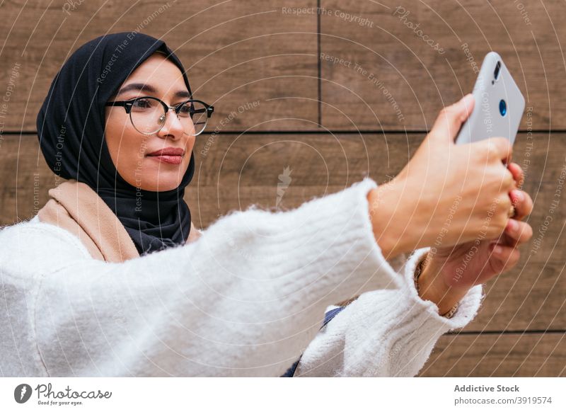 Charming ethnic woman in hijab taking selfie in city headscarf smartphone take photo memory smile charming female arab street photography self portrait using
