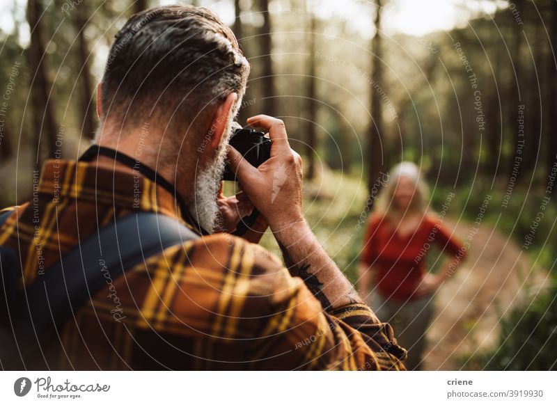 Senior man taking photo with camera of woman in forest senior mature together hiking lifestyle leisure outdoors