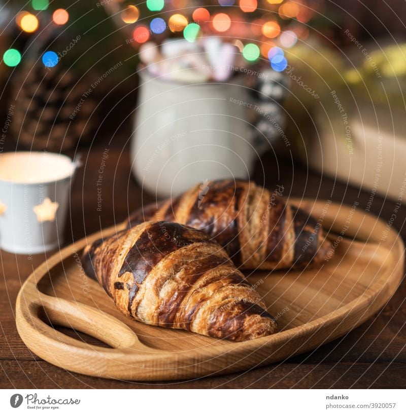 baked croissants and a white ceramic cup with coffee, behind the burning Christmas lights mug new year pastry roll rustic snack sweet decor delicious dessert