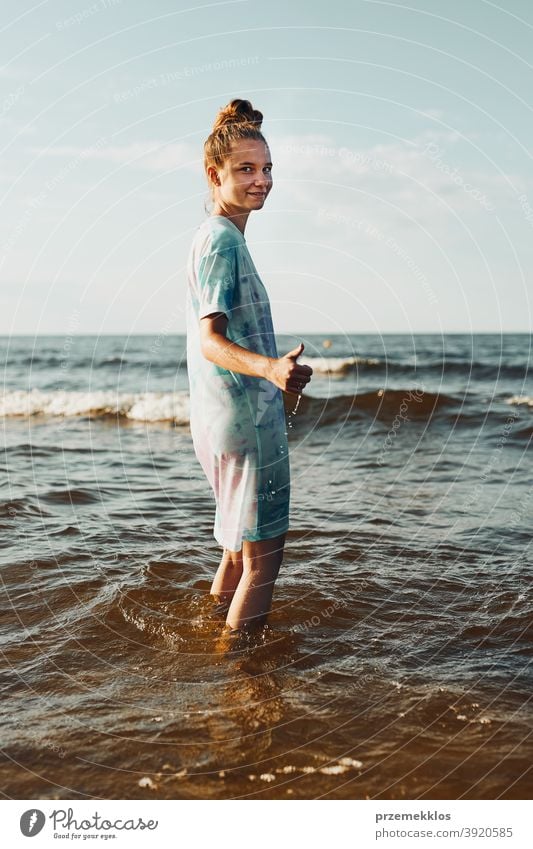Girl showing okay gesture standing in a water spending a free time over a sea during summer vacation excited enjoy positive sunset emotion carefree nature