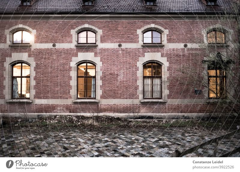Frontal view on brick building with four large and four small windows Window red bricks Cobblestones Paving stone evening mood House front