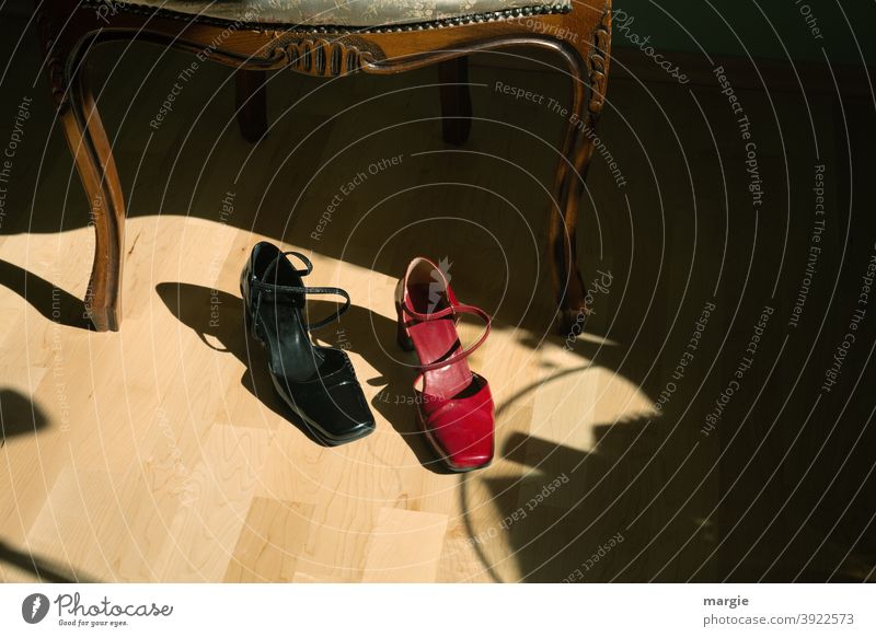 A pair of ladies - shoes in front of a chair, one shoe is red, the other black Footwear Chair floor Parquet floor Red Black Interior shot Deserted