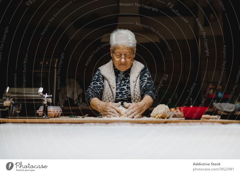 Aged woman kneading dough in kitchen cook raw italian food tortellini tradition homemade dumpling female senior housewife cuisine aged prepare tasty table fresh