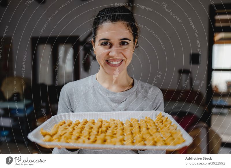 Content woman with tortellini on baking pan cook homemade tradition italian food dumpling dough raw female smile prepare ingredient cheerful table