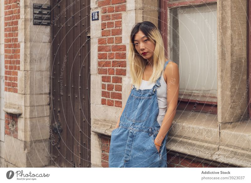 Stylish ethnic woman standing on street denim overall style city trendy confident apparel summer urban female asian building personality modern outfit slim lady