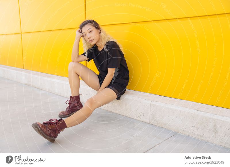 Young ethnic woman sitting near yellow wall hipster young urban street style color teen modern female asian dyed hair teenage millennial lifestyle adolescent