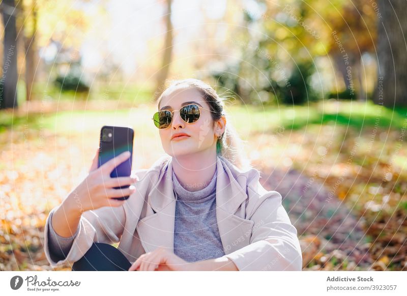 Positive woman sending message on mobile phone in park smartphone enjoy cheerful autumn female gadget content device cellphone happy optimist lady glad