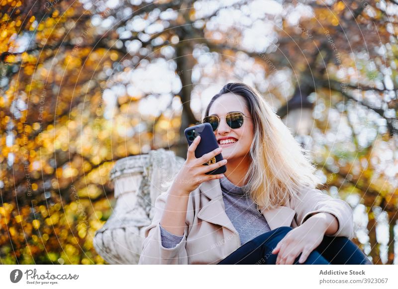 Positive woman sending message on mobile phone in park speak smartphone enjoy conversation cheerful autumn female gadget content device cellphone happy optimist