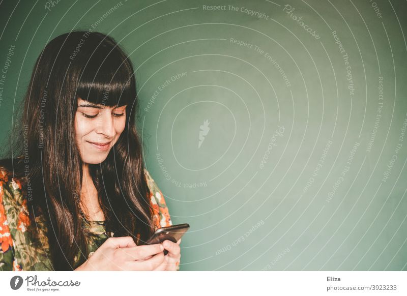 Consumer terror | A brown-haired young woman types something on her mobile phone and smiles. Cellphone Telephone Smiling Typing copywriting Write smartphone