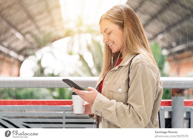 Smiley Girl Looking at Phone side view looking at phone cup of coffee headphones girl portrait young 20s blonde pretty using phone cellphone caucasian standing