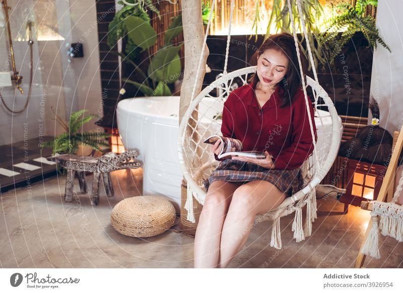 Ethnic woman with magazine relaxing in chair read rest hotel chill traveler cozy rope hang young asian female ethnic taiwan lifestyle holiday vacation comfort