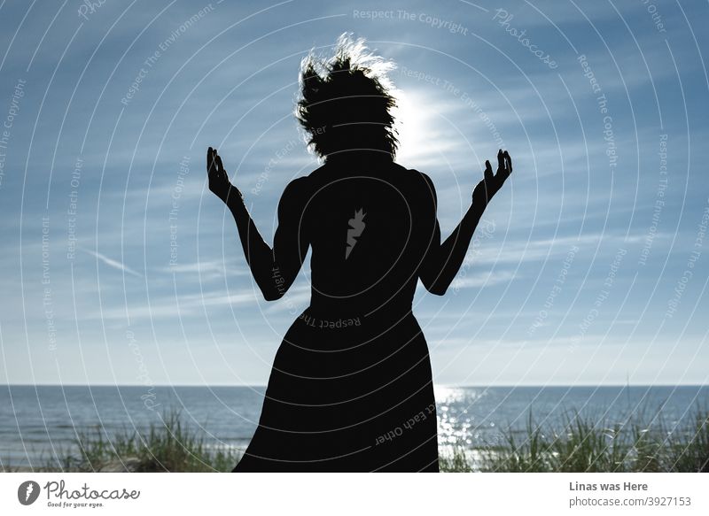 Blue sky and water of the sea is blue as well. Sun is shining bright in the middle of a perfect summer day. A dark silhouette of a wild woman is in front of a camera. Some dramatic action is happening.